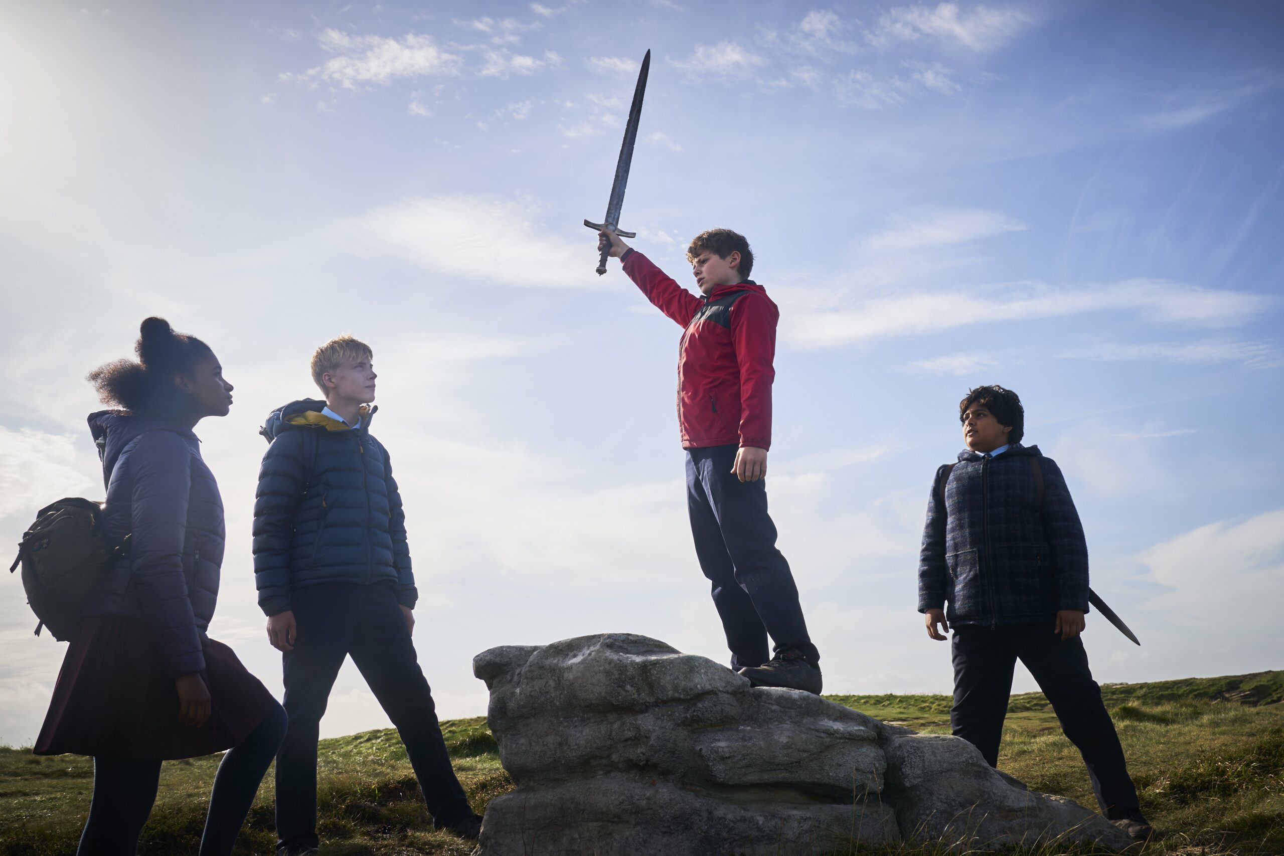 Louis ashbourne Serkis as Alex, standing on a rock holding up a sword
